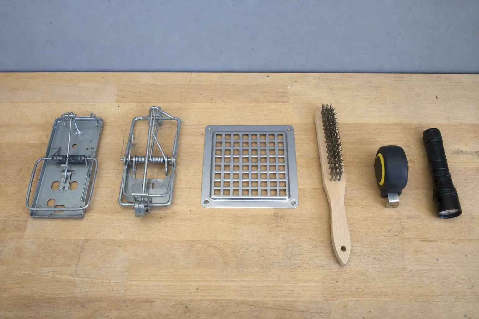 Pièges mécaniques, grille d'obturation, brosse métallique et lampe d'inspection alignés sur un établi